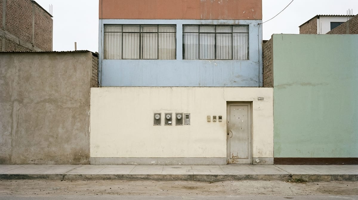 Fachada de una casa familiar de tres pisos en Lima, cada piso pintado de un color distinto, con tres medidores de luz juntos en la pared