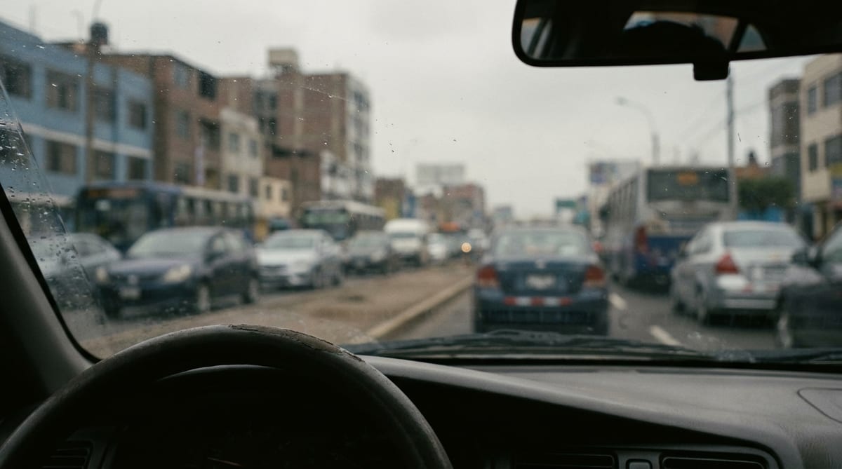 Vista desde el interior de un auto detenido en una avenida de Lima, con el espejo retrovisor y el tráfico desenfocado al frente