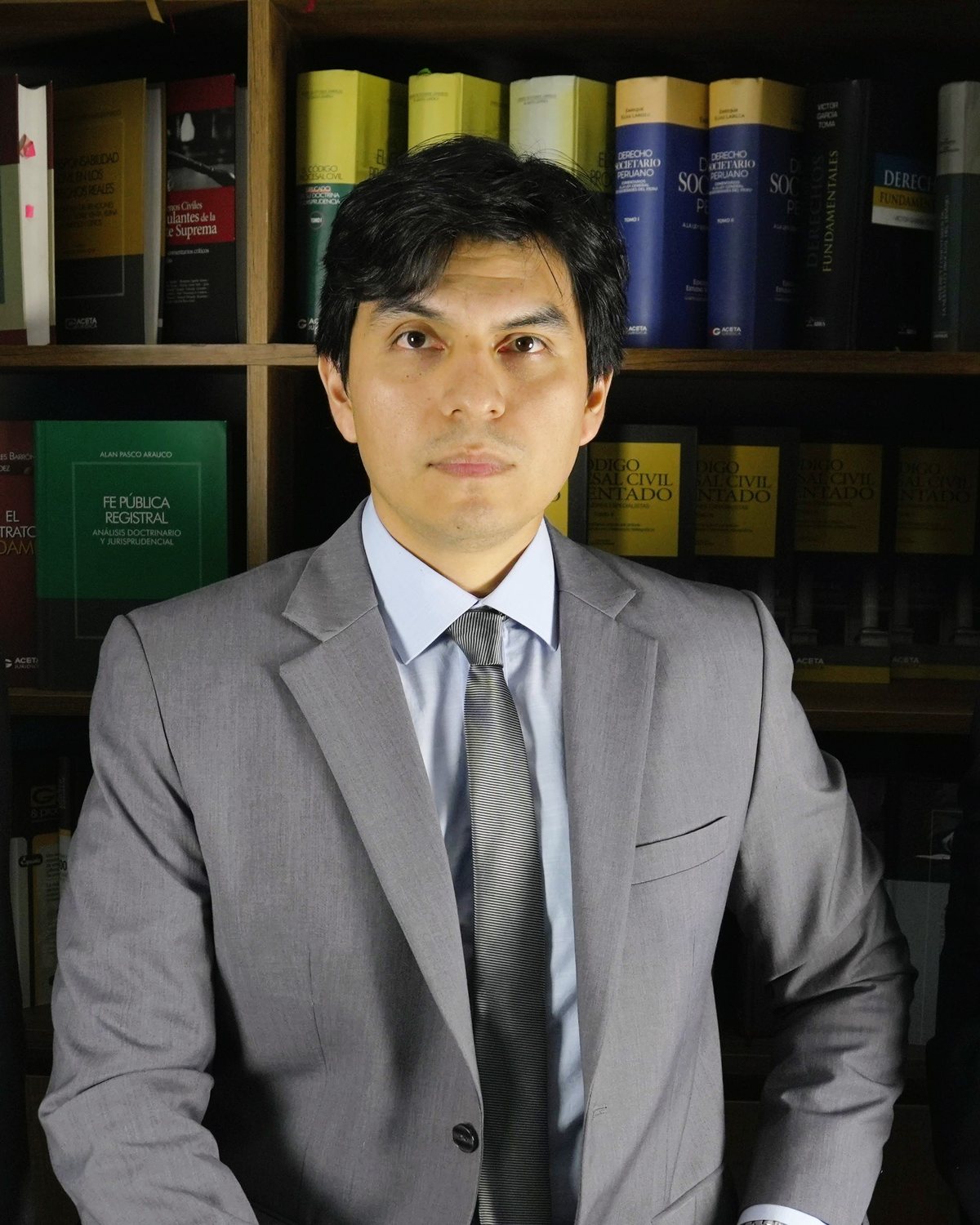 Retrato de Paul Arroyo, abogado, con traje gris frente a una biblioteca jurídica